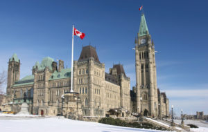 Photo of the houses of parliament in Ottawa on a sunny day with snow on the ground.