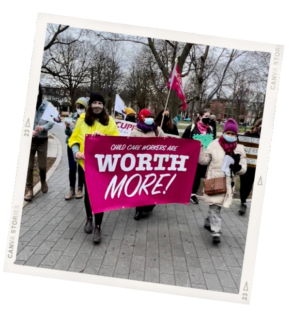 A photo of a protest with a pink banner that says Child Care Workers Are Worth More