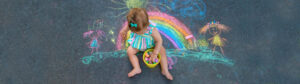 Baby draws a rainbow on the pavement with chalk.