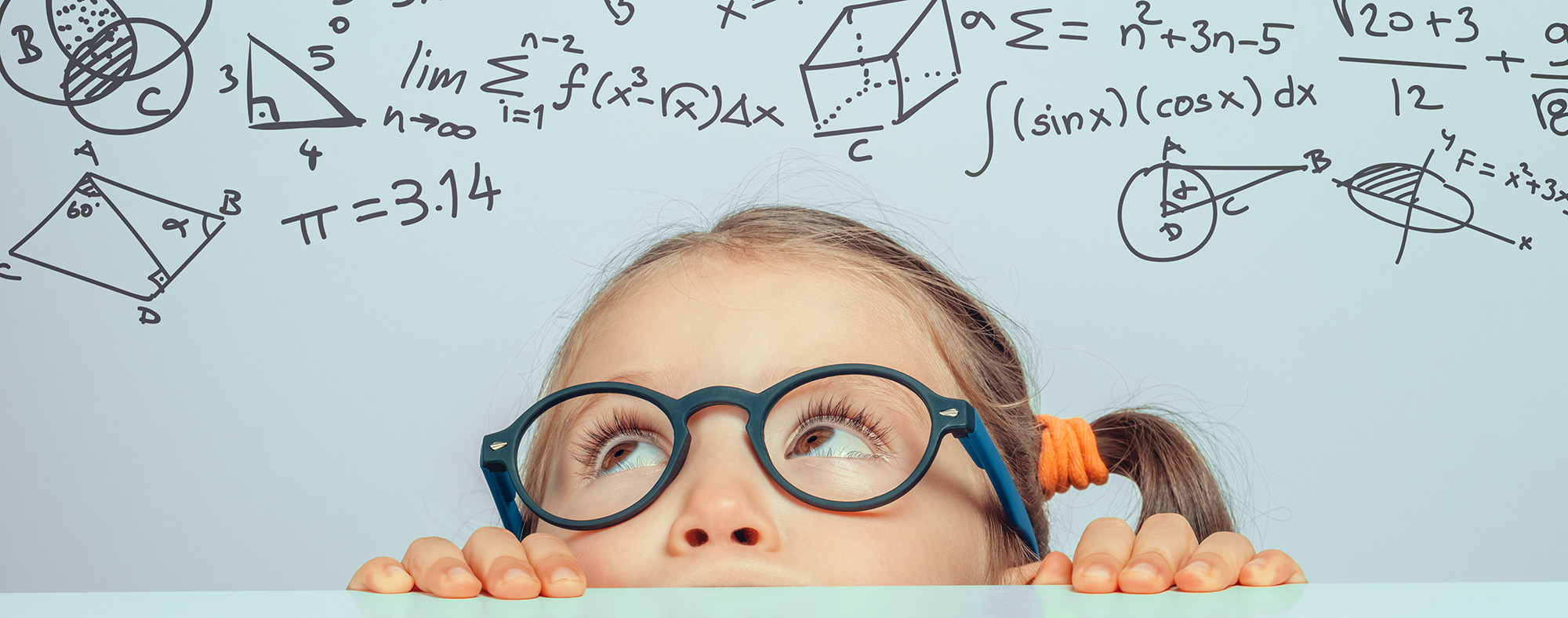 little girl peeking over a table looking up towards math formulas and problems on the wall above her