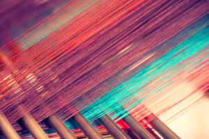 A close up of orange and turquoise threads being woven.